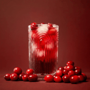 Harvest Valley Cranberry Juice served in a glass with cranberries sitting around the glass on a dark maroon background.