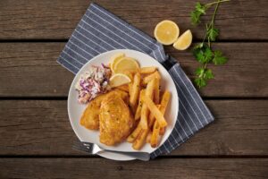 Plate of lemon pepper beer battered fish with lemons next to it and green garnish