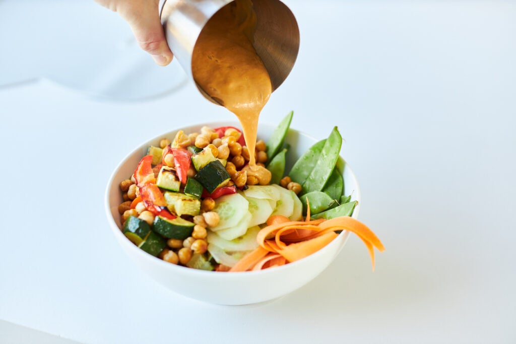 Pouring sauce on top of the Trade East Lemon Pepper Buddha Bowl