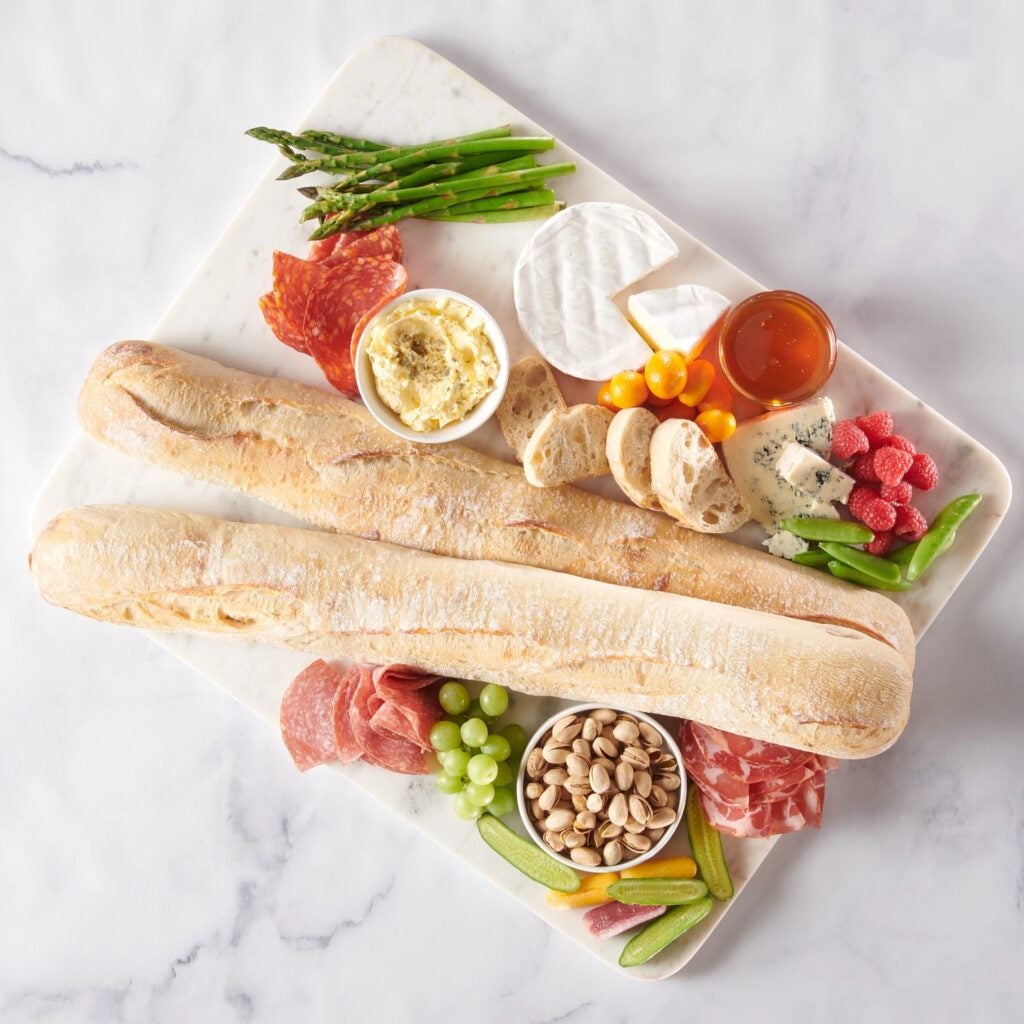 Deux baguettes françaises entourées de viandes, de fromages, de noix et d’autres ingrédients.