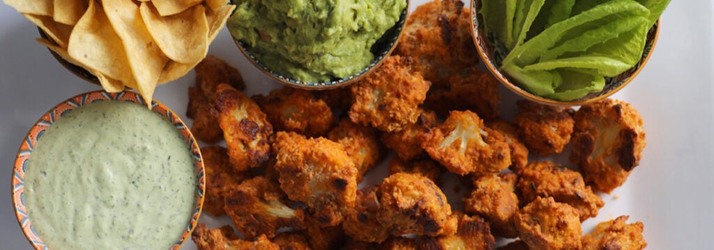 Buffalo cauliflower with guacamole, green sauce, lettuce, and chops served on the side