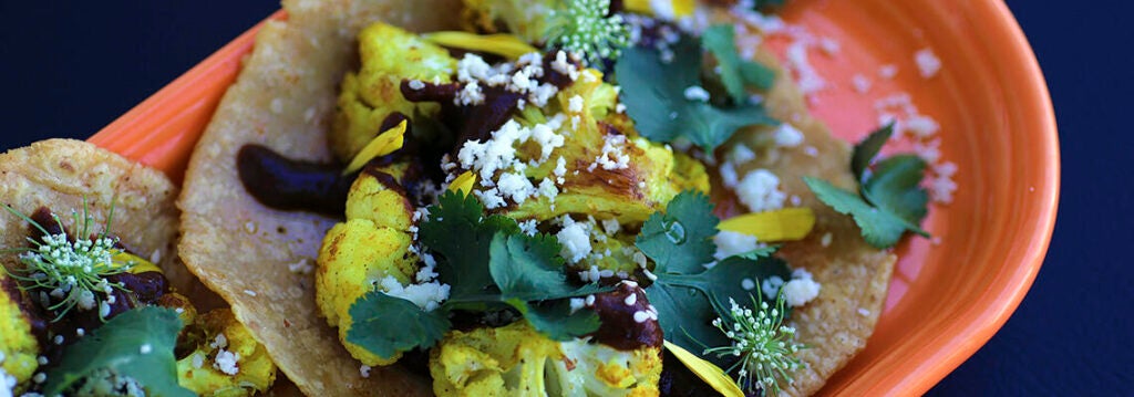 Cauliflower tacos served with greens on a corn shell in an orange dish.