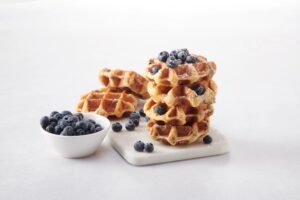 A stack of waffles covered in fresh blueberries.
