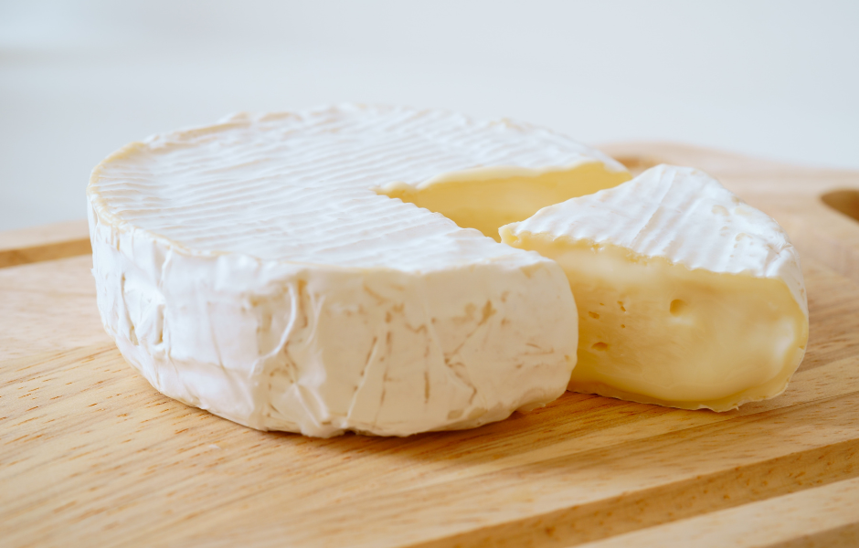 Soft ripened Camembert cheese wedges served with a spoonful of creamy brie on a rustic wooden board.