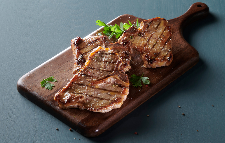 Grilled pork chops seasoned with sea salt and fresh parsley served on a dark wooden cutting board.