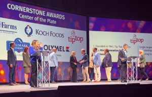 People gather on stage during the Cornerstone Awards presentation held in front of sponsor logos.